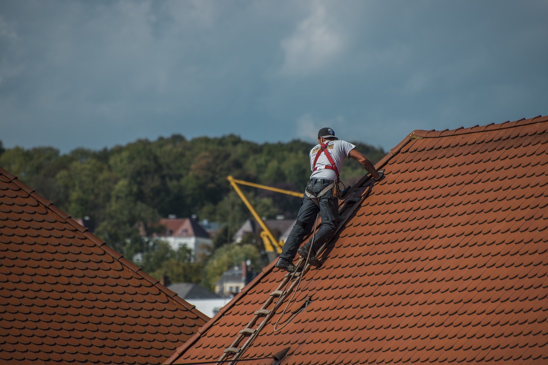 roofer using harness and safety equipment on red tile roof